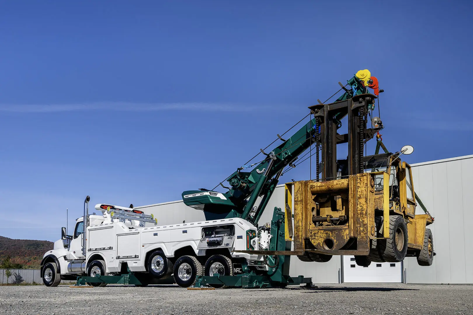Tow truck lifting large yellow machinery.