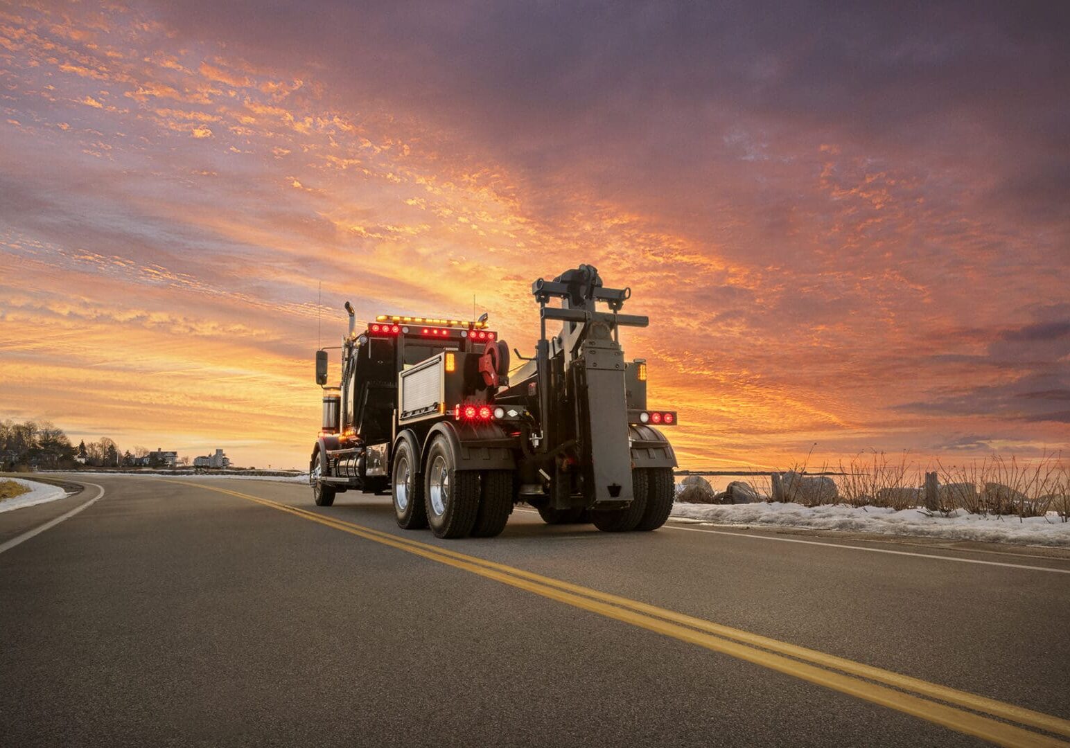 Tow truck on road at sunset.